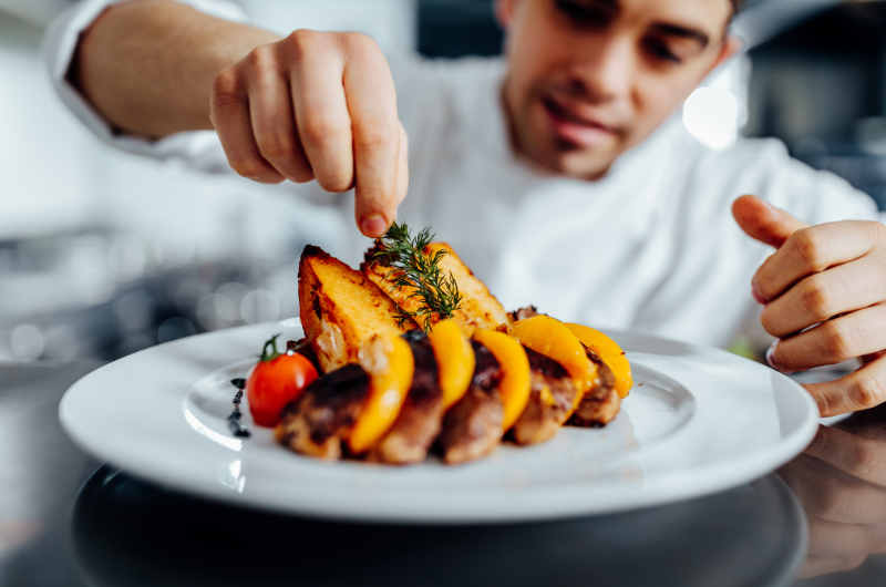 A young chef decorates a plate with a dish of melon on it
