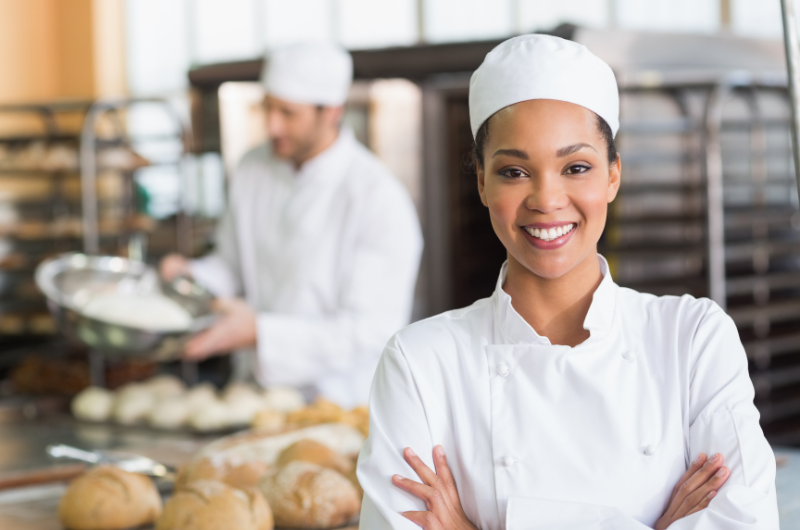 Cook stands in a kitchen and smiles at the camera with her arms crossed